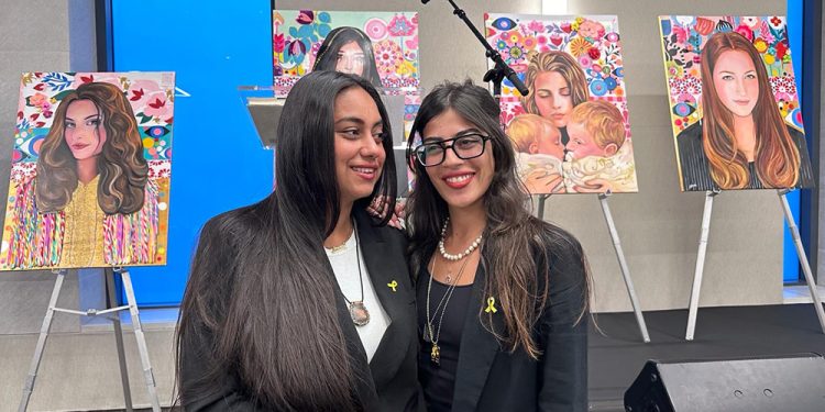 מיכל ואבישג באחת ההרצאות שנתנו בעיר. ברקע, ציורים של החטופים אותם ציירה ג'סיקה לבטון פרסון  ניצולות נובה מספרות על היום ששינה את חייהן